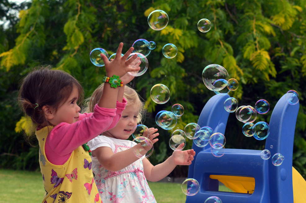 Two young children playing with bubbles outdoors on a sunny day
